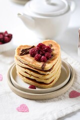 Pancakes in the shape of a heart with chocolate cream, lie on top of each other, decorated with raspberries. Breakfast for Valentine's Day.
