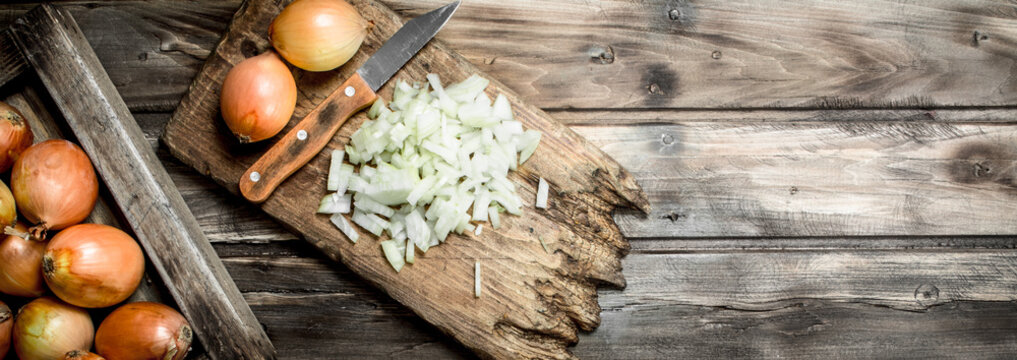 Pieces of onions on a cutting Board with a knife and a whole onion on the tray.