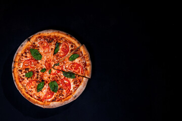 Delicious fragrant pizza-Margherita with mozzarella, tomatoes and basil on tomato sauce on black background. Copy space