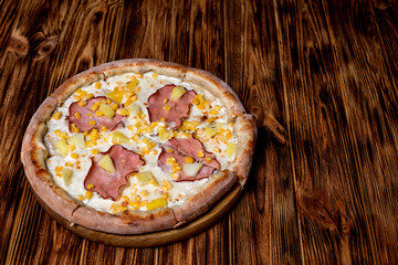 Delicious pizza with ham, pineapple, corn on a creamy base on woden background. Hawaiian pizza