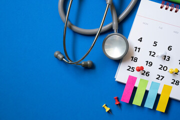 Top view of stethoscope and calendar on the blue background, schedule to check up medical healthy concept