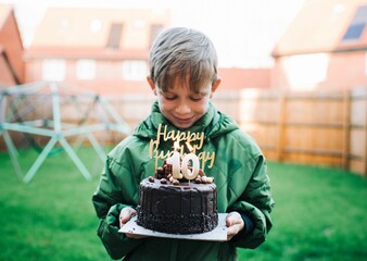 boy happily holding his 10th birthday cake with candles at home