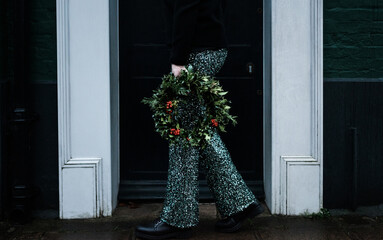 Woman holding Christmas wreath with sparkly trousers on
