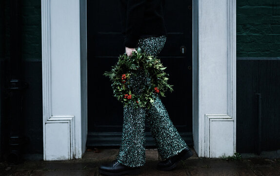 Woman holding Christmas wreath with sparkly trousers on