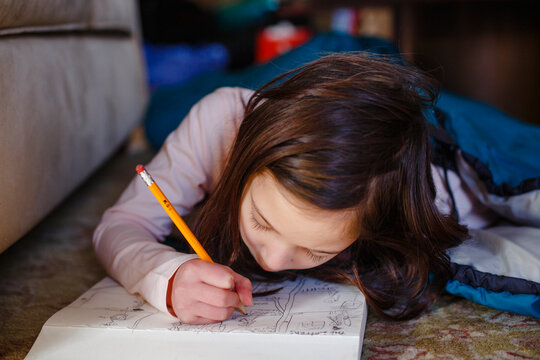A little girl laying on floor draws carefully in sketchpad