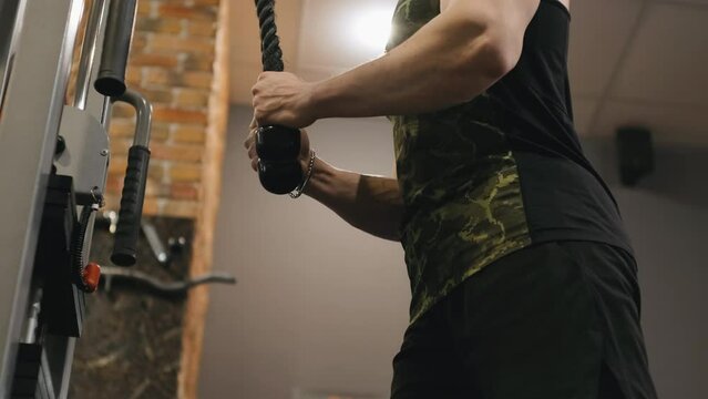 Muscular trainer doing cable triceps pushdown gym machine