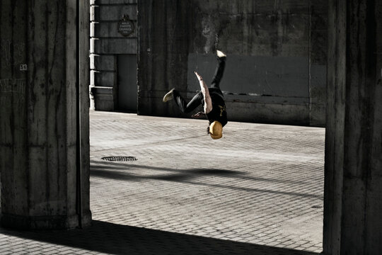 Young adult doing a somersault while breakdancing under a bridge in Bilbao, Spain.