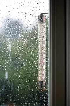 Rain seen through a window with a  thermometer  showing 15 degrees.