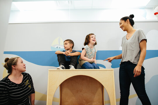 Teachers interact with two students sitting on top of a cube