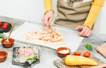 Hands of a caucasian teenage girl in an apron cut out the dough in the shape of a heart for pizza.