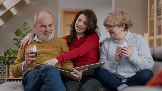 Young female sitting laughing with grandparents sharing memories looking through photo album