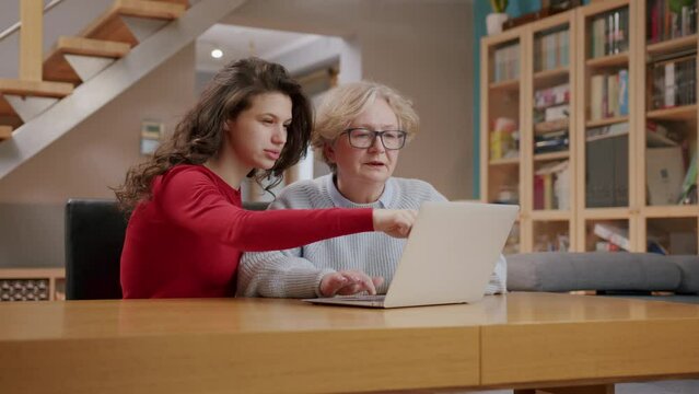 Attractive young lady with red cardigan helps grandmother on laptop; living room
