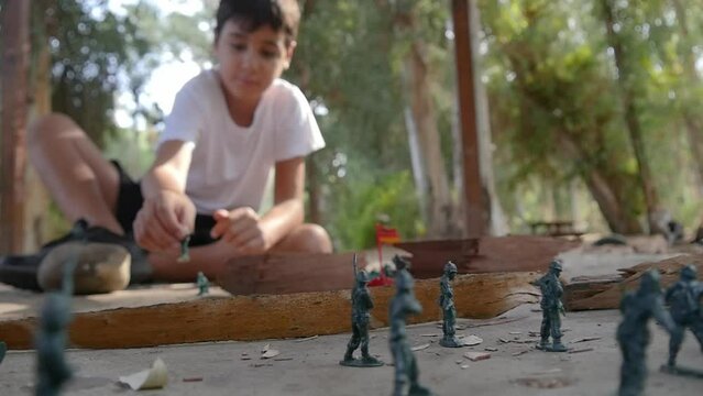 A boy plays alone with plastic green army men at the park.