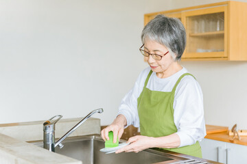 家のキッチンでお皿洗いをするシニア・高齢者女性（疲労）