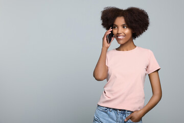 Smiling African American woman talking on smartphone against light grey background. Space for text