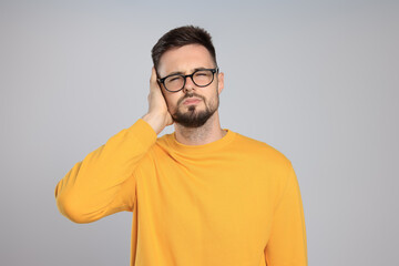 Young man suffering from ear pain on light grey background