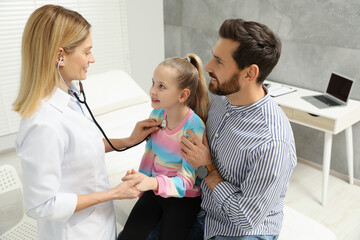 Father and daughter having appointment with doctor. Pediatrician examining little patient with stethoscope in clinic