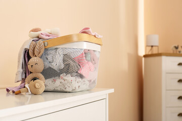 Laundry basket with baby clothes and crochet toys on white chest of drawers indoors, space for text