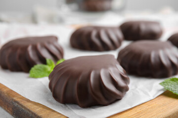 Delicious chocolate covered zephyrs and mint on wooden board, closeup