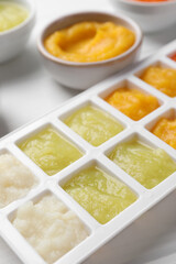 Different purees in ice cube tray on white table, closeup. Ready for freezing