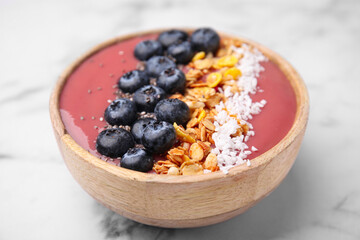 Bowl of delicious fruit smoothie with fresh blueberries, granola and coconut flakes on white marble table, closeup