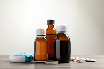 Bottle of syrup, dosing spoon and pills on table against light background. Cold medicine