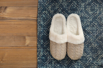 Pair of beautiful soft slippers and rug on wooden floor, top view. Space for text