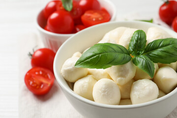 Delicious mozzarella balls and basil leaves in bowl on table, closeup