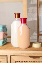 Solid shampoo bar and bottles of cosmetic product on wooden table in bathroom