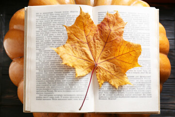 Naklejka na ściany i meble Book with autumn leaf as bookmark and ripe pumpkin on table, top view