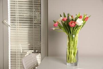 Beautiful bouquet of colorful tulips in glass vase on table at home
