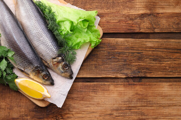 Board with delicious salted herrings, lemon and herbs on wooden table, top view. Space for text