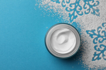 Jar of hand cream and snowflakes on light blue background, top view with space for text. Winter skin care
