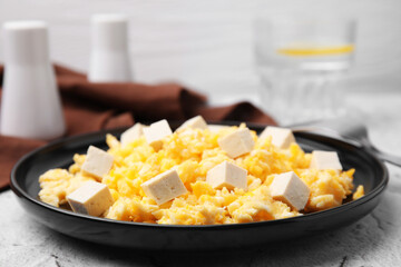 Plate with delicious scrambled eggs and tofu on white textured table