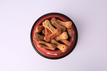Bone shaped dog cookies in feeding bowl on white background, top view