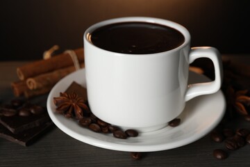 Cup of delicious hot chocolate, spices and coffee beans on wooden table