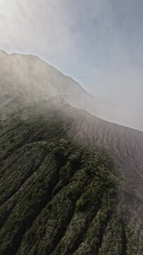 Tropical island volcano smoke panorama stone crater with mist gas steam sea landscape aerial view. FPV sport drone shot cinematic seaside exotic scenery volcanic acid lake mountain. Vertical video 4k