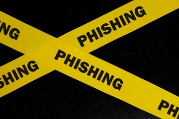 Phishing scam alert, caution and warning concept. Yellow barricade tape with word phishing in dark black background.