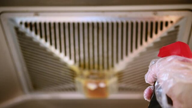 man spraying chemical liquid to an oily filter hood of a kitchen ventilator at horizontal composition
