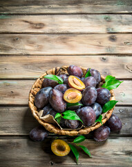 Halves and whole plums with leaves in the basket.