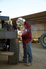 Fototapeta na wymiar Welder in Front of Barn Melting Metal in Protective Wear