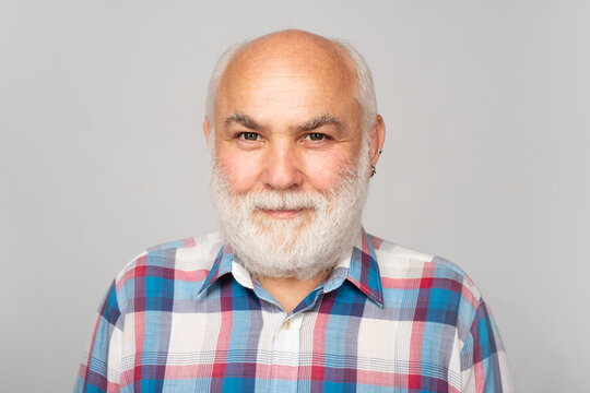 Elderly Caucasian Old Man Face. Old Mature Senior Man With Grey Beard On Grey Studio Background. Portrait Of An Bald Old Mature Senior Man With Grey Beard In Shirt Isolated On Gray Studio Background.