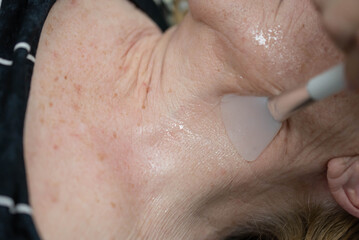 Elderly woman on facial massage procedure at cosmetology clinic.