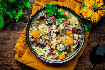 Winter comfort food. Warming soup with pumpkin, mushrooms, vegetables, beef and barley. Rustic wooden table background, top view