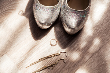 Bride's shoes, ring and earrings on a wooden floor in the sun. Top view