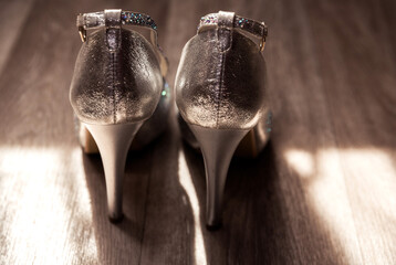 Beautiful women's shoes of silver color stand on a wooden floor in the sun. Back view
