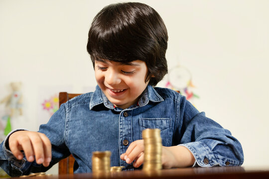 Young smart boy counting his coins/savings to buy dream toys - Saving concept. Stock image of an adorable child boy wearing casual dress is sitting on a chair while counting his savings