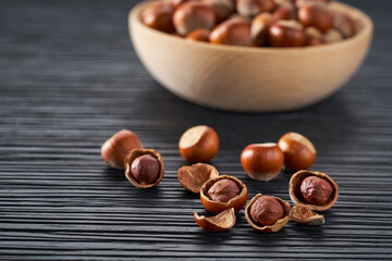 hazelnut spill out of a wooden bowl on a black table, selective focus.