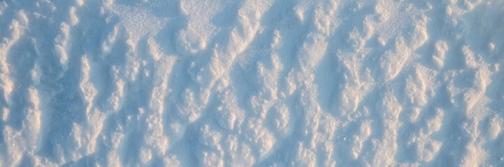 Beautiful winter background with snowy ground. Natural snow texture. Wind sculpted patterns on snow surface. Wide panoramic texture for background and design.