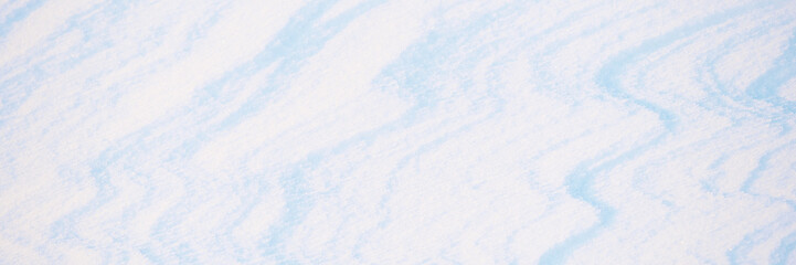 Wide panoramic winter background with snowy ground. Natural snow texture. Wind sculpted patterns on snow surface.